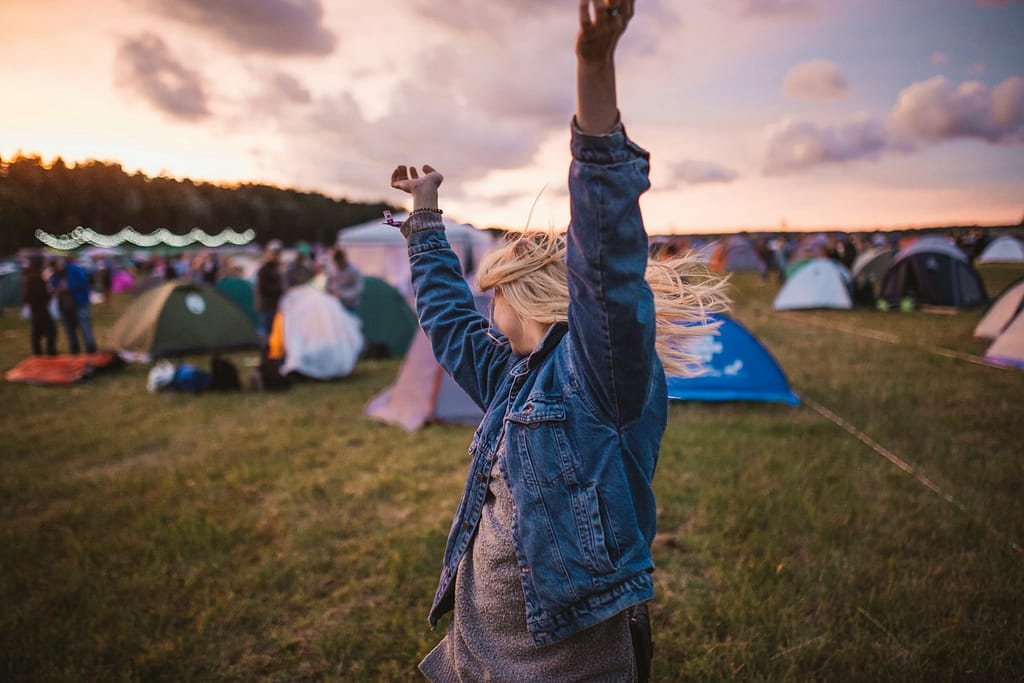 a woman raising her arms in the air in front of tents at a free festival uk 